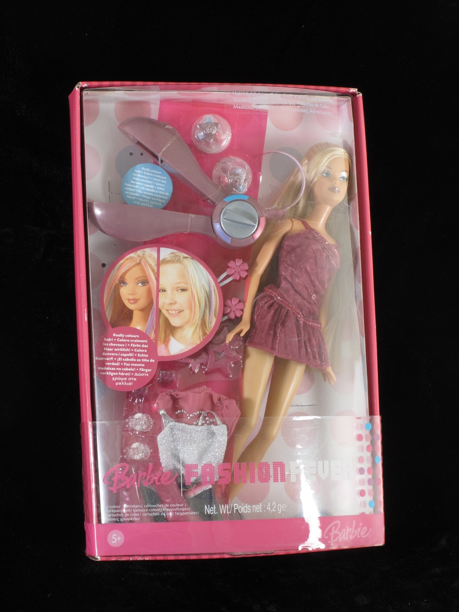 Barbiedokke med lyst, langt hår. Ikledd mørk rosa kort kjole. I esken ligger også hårbørste, rekvisitter til hårpynt, hårføner, støvler m.m. Alt ligger i uåpnet originaleske. Esken har rosa kanterog lokk i klar plast.
