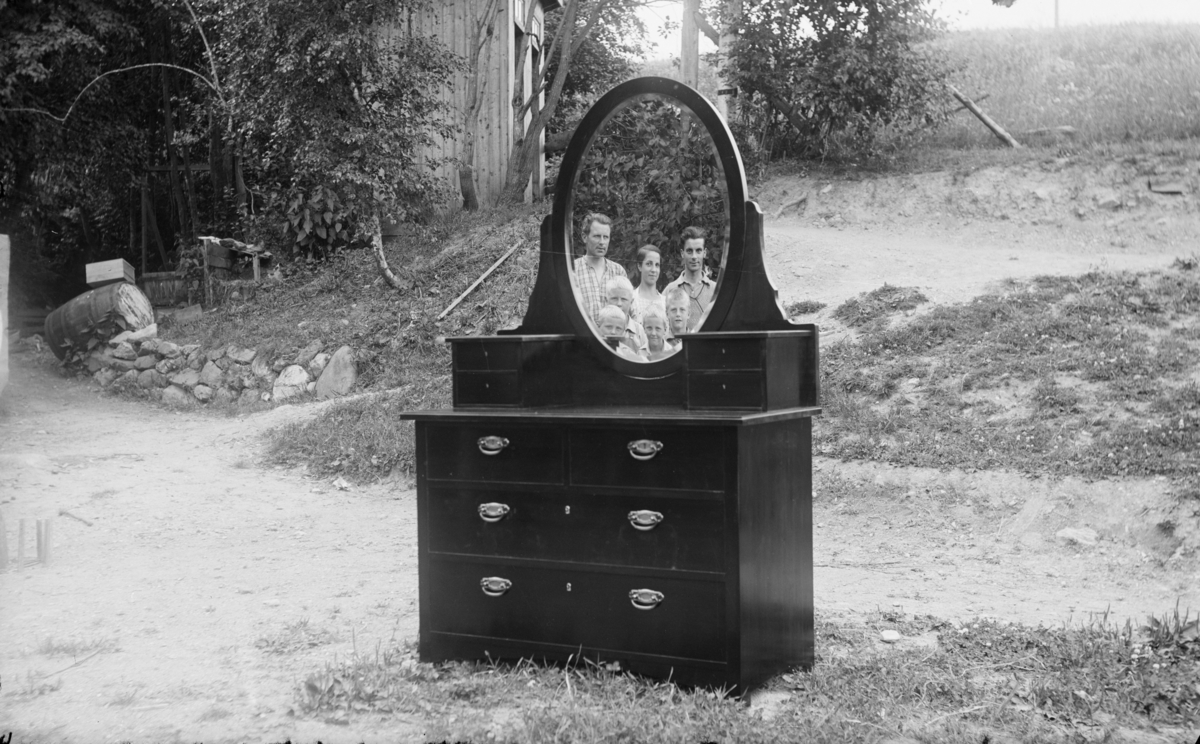 En kommode med speil plassert utenfor et hus. Familiebilde  reflektert kommodespeilet.