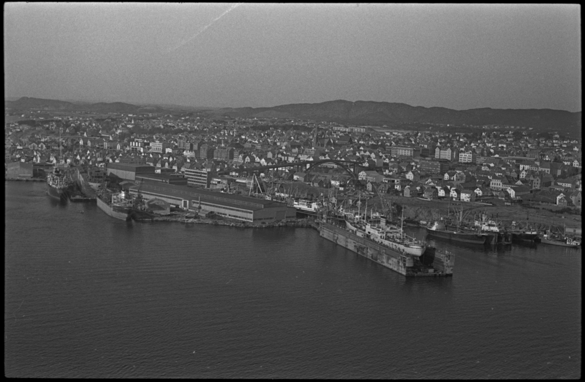 Haugesund Mekaniske Verksted sett fra vest. Det er skip i produksjon både i tørrdokken og i flytedokken og flere skip ligger til kai. Haugesund ligger i bakgrunnen.