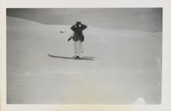 Mann med gevær på rygge står på ski i fjellet og ser med kik