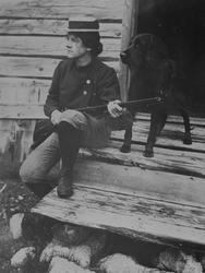 Fru Margit Kielland med jaktvåpen og hund avbildet ved innga