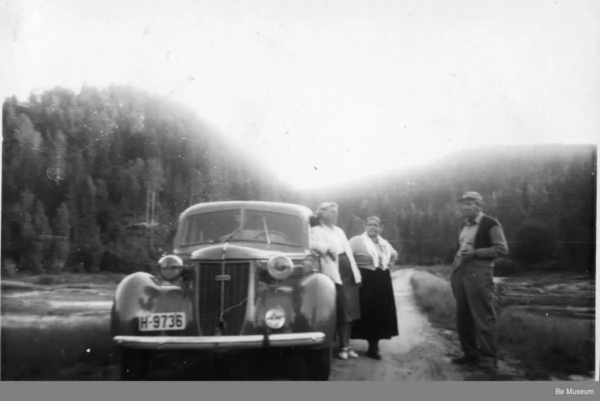 3 personar og ein bil fotografert ved Holmstul.  H-9736 er ein Wanderer frå seint 30-tall. Bildet må vere tatt etter at Telemarks Bileiere 1938 kom ut. Høgste registreringsnummer i   denne serien for Bø lensmannskontor var då H-9695.