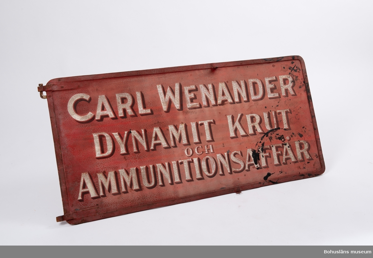 Text å båda sidor i vitt och svart mot botten i engelskt rött: 
"Carl Wenander. Dynamit, -Krut och Ammunitionsaffär."