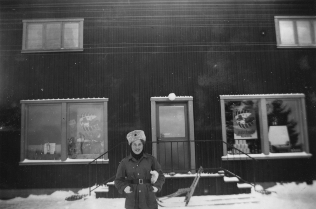 En kvinna i militär uniform står utanför en livsmedelsbutik i Kåbdalis, vintern 1942. Affären är en Konsumbutik.