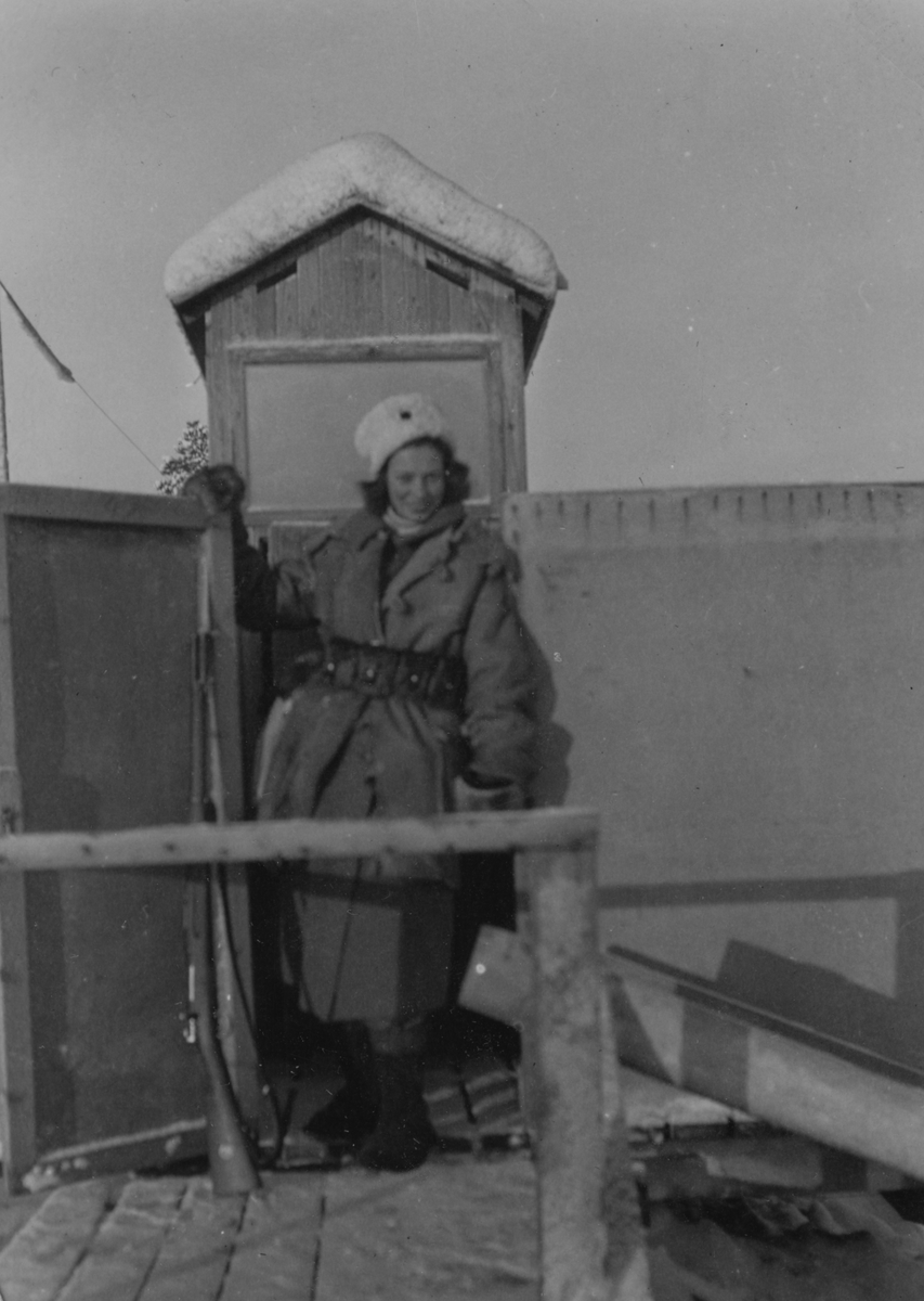 Porträttfoto av Sally Svensson, kvinnlig luftbevakare stående i ett luftbevakningstorn vintertid, 1942. Klädd i uniform och med gevär.  Sally tillhörde 91:a ls-kompaniet i Tellejåkk, Kåbdalis under beredskapsåren.