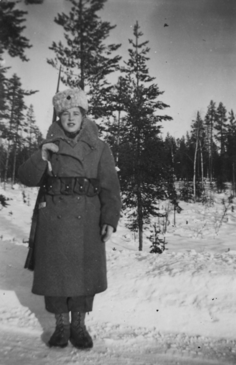 Porträtt av luftbevakare Karin Nordberg i uniform och med gevär, vintern 1942. Utomhus vid luftbevakningsförläggningen tillhörande 91:a ls-kompaniet, Tellejåkk, Kåbdalis under beredskapsåren.