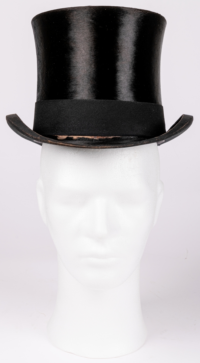 Hög hatt med kraftigt uppsvängda brätten, märkt B.L. ink. hos firma J.W. Haglund, Gefle.
Tillhörande hattask.