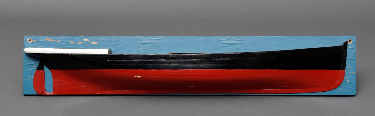 Halvmodell av skipet DS "Fram" festet på en blåmalt bakplate. Gjennomgående skruehull for veggmontering. Modellen er laget av tre, og er malt i sort og rødt.