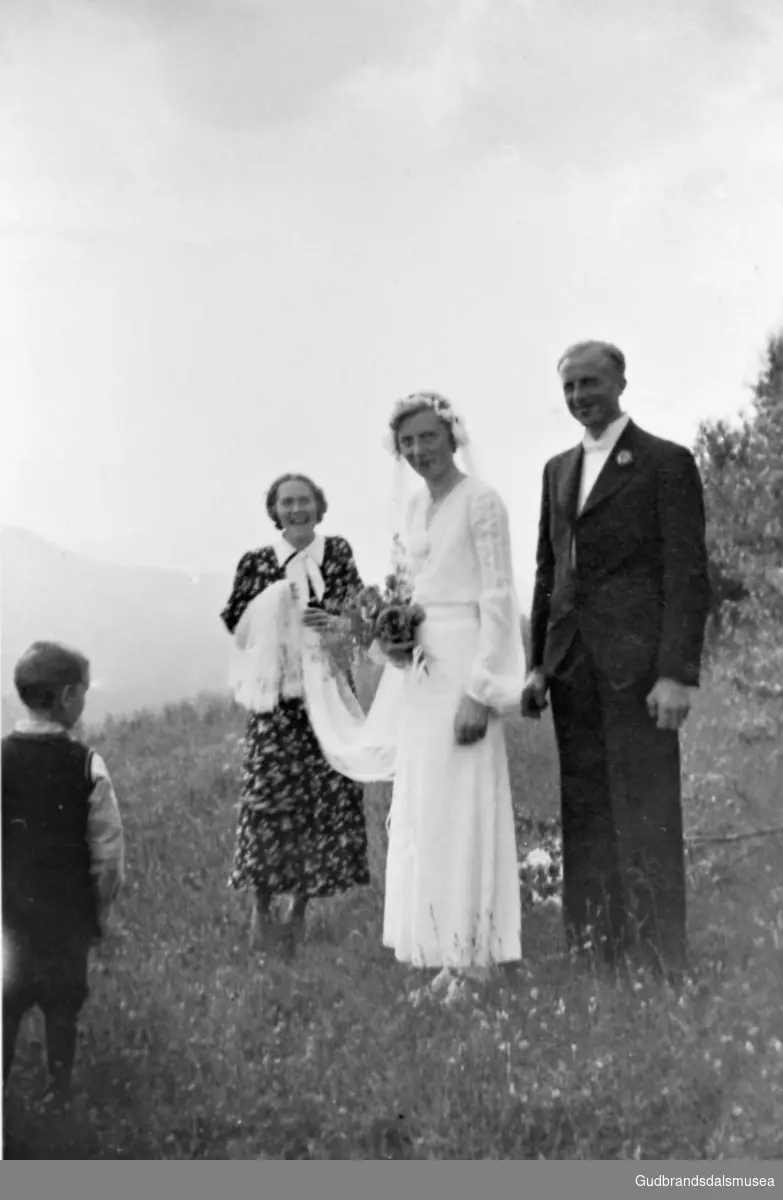 Portrett, brudeparet fotografert ute på jordet på Nørdre Plassen, kvinne og gutt står rundt.

