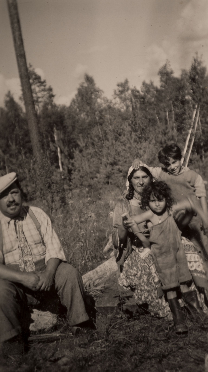 En grupp romer har slagit sig ned för att bli avfotograferade. Två barn klänger på en kvinna och en man sitter bredvid. Bilden är tagen i Hofors 1950.