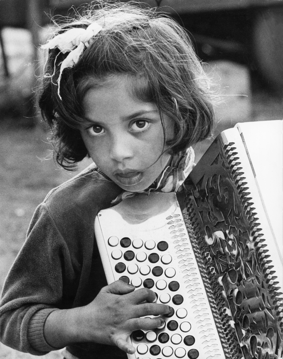 En romsk flicka tar ett ackord på ett knappdragspel. Flickan bär en rosett i håret.