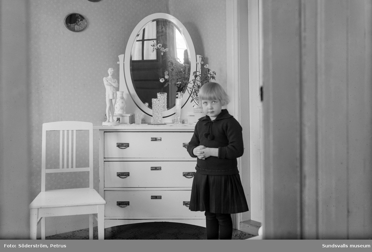 Två porträtt på Märta Johansson, Bjällsta. På bild 1 leker hon med en hund på brokvisten. På bild 2 står hon vid en spegelbyrå.