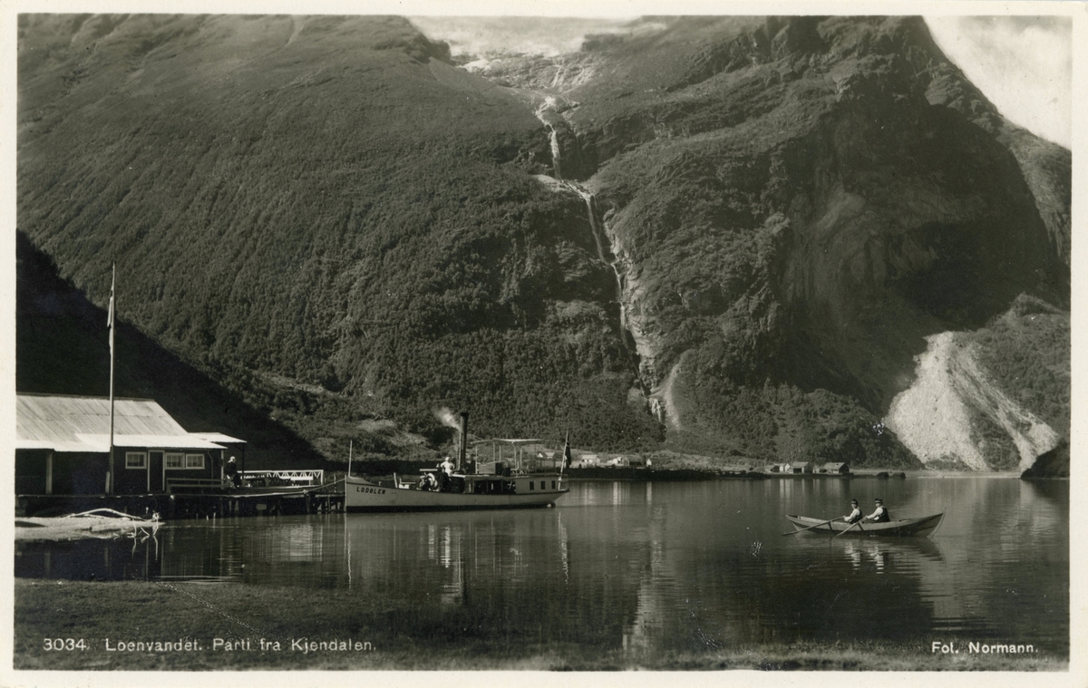 Motiv av dampbåten D/S "Lodølen" på Lovatnet ved Kjenndalen. To menn i en robåt i forgrunnen.