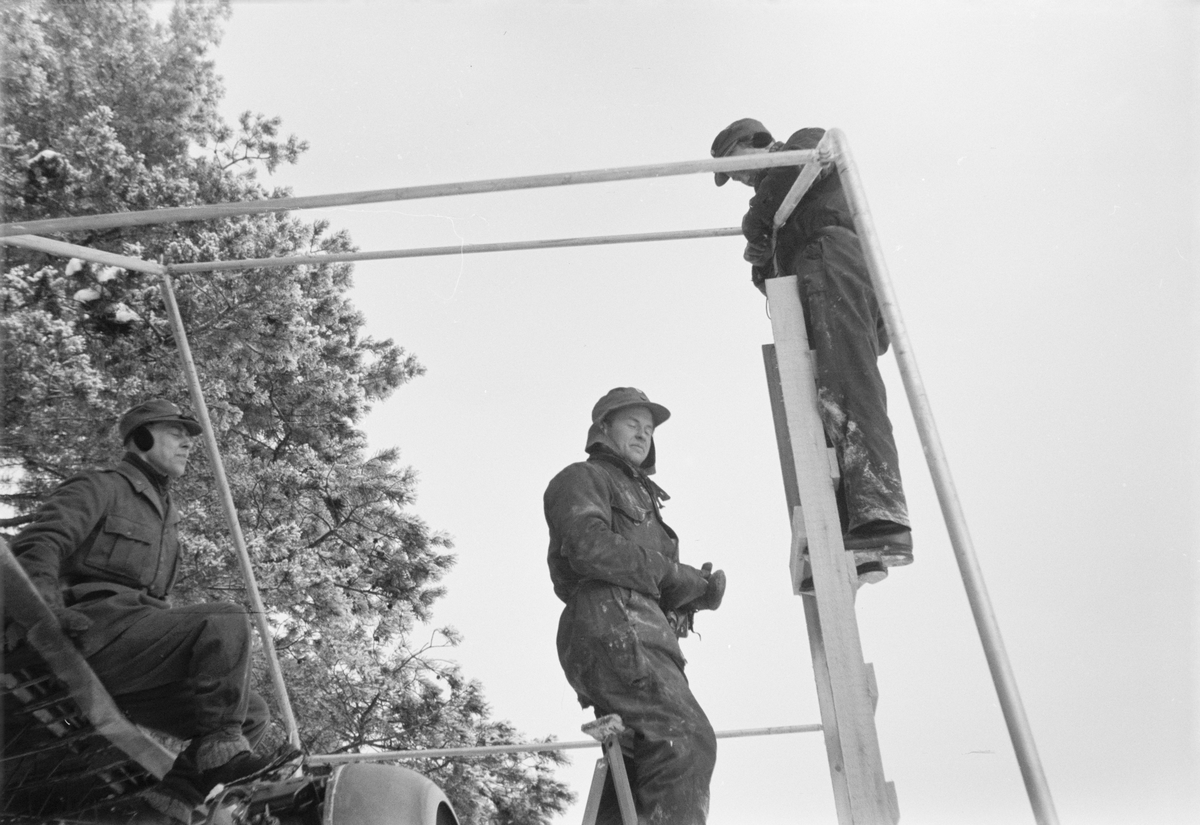 Skyddstält för flygplan Gloster Gladiator sätts upp vid F 19, Svenska frivilligkåren i Finland, 1940. Tre män i arbete. Närbild.