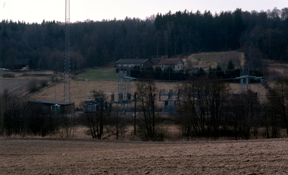 Vy över odlingsmark, Fortums (senare Ellevios) elkraftverk samt Heljered Västergårdar år 1978. Sandsjöbacka naturreservat ses i bakgrunden.