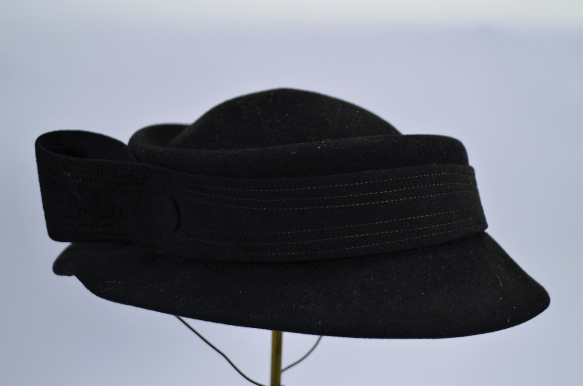 Hatt i mørk blå fløyel, pynta med blått ripsband og perler. 
Ripsband rundt kanten inni, og hattestrikk for å feste hatten.
