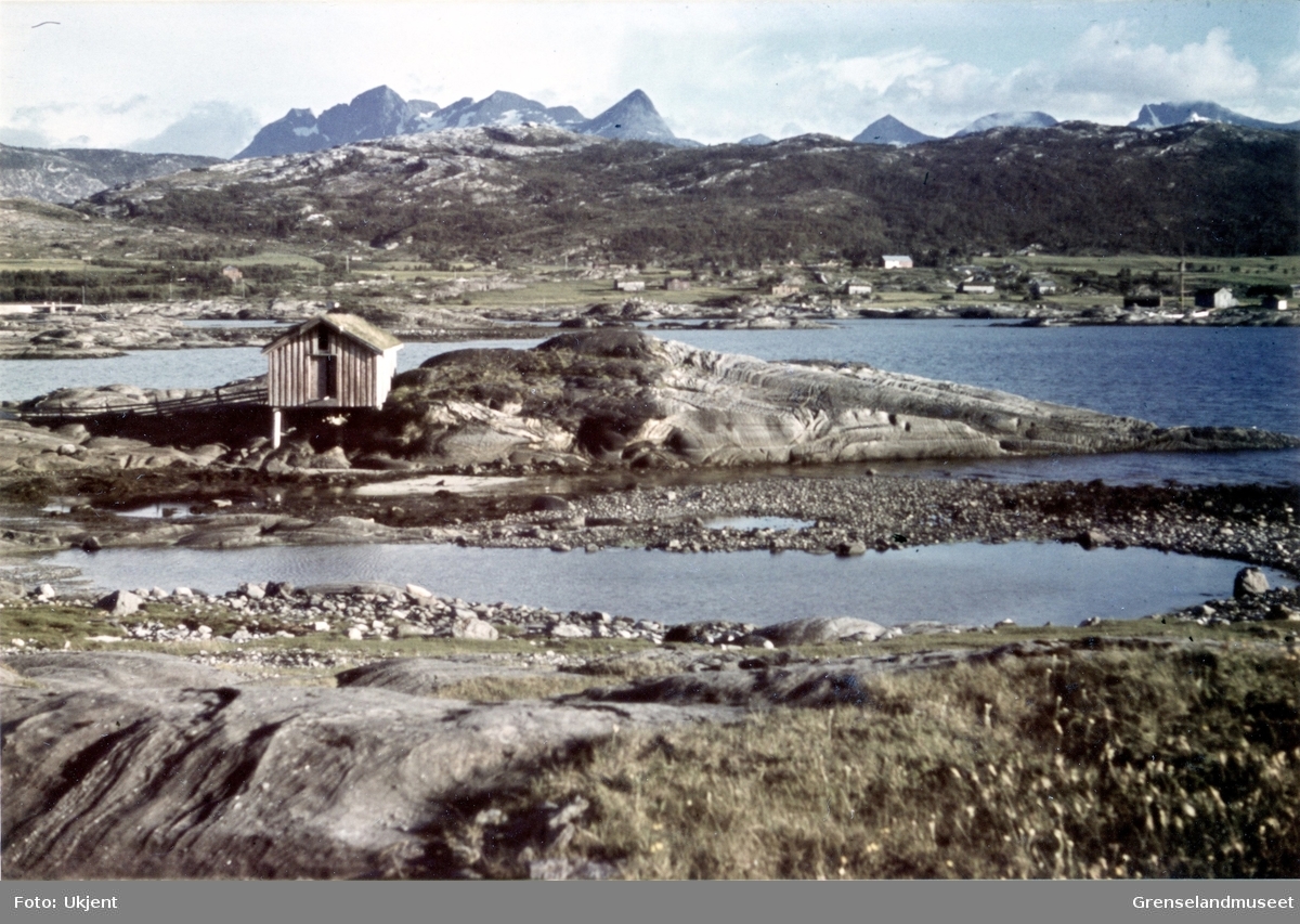 Motiv fra Saltenfjorden i Nordland. Bøvasstindan i bakgrunnen. Spredt bebyggelse midt i bildet.