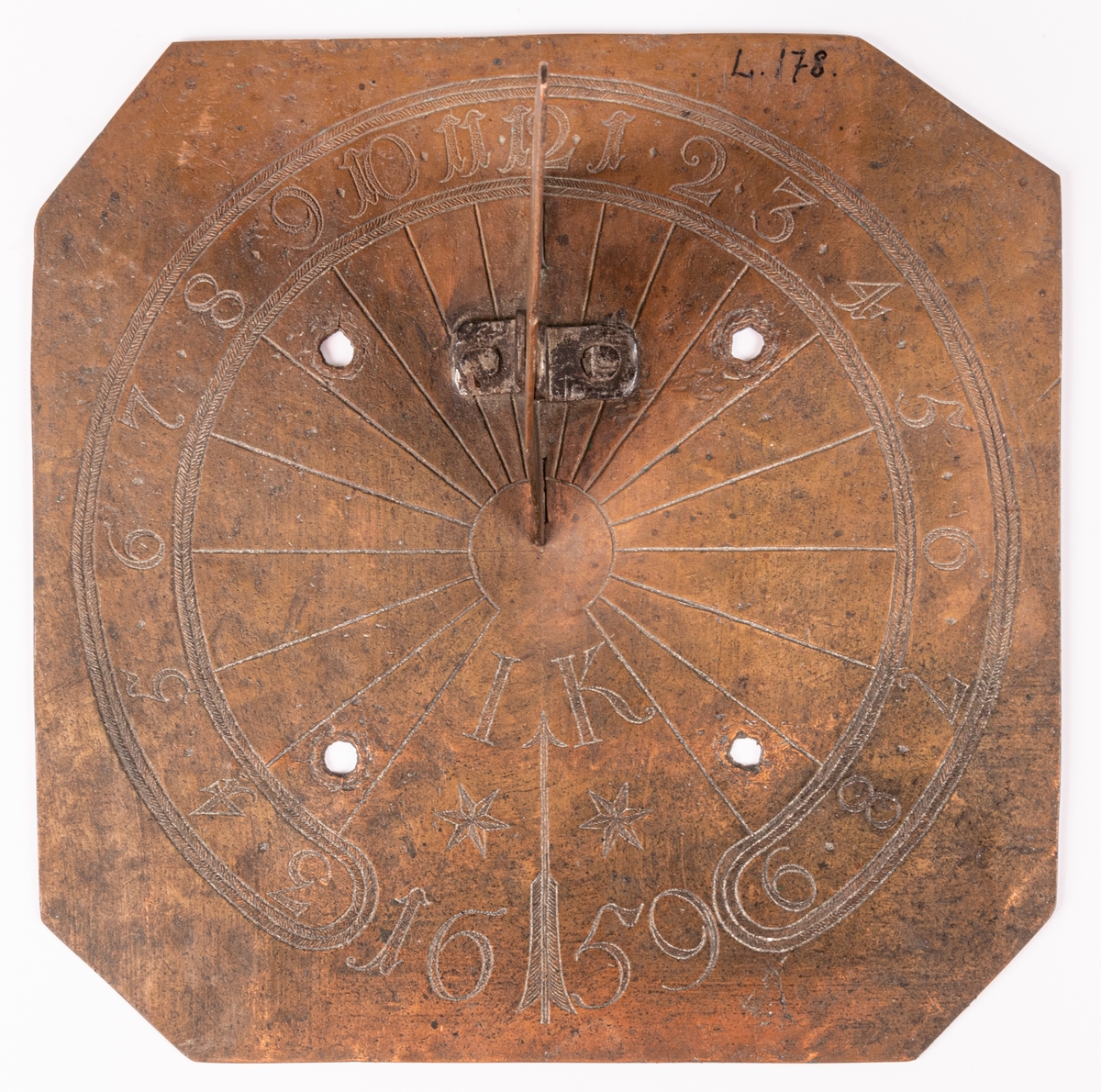 Solvisare av koppar, fyrsidig med triangulär stående visare. Fyra borrade hål för skruvar. Ristat cirklar med timsiffror och radiära linjer från centrum.  Märkt: "IK 1659".