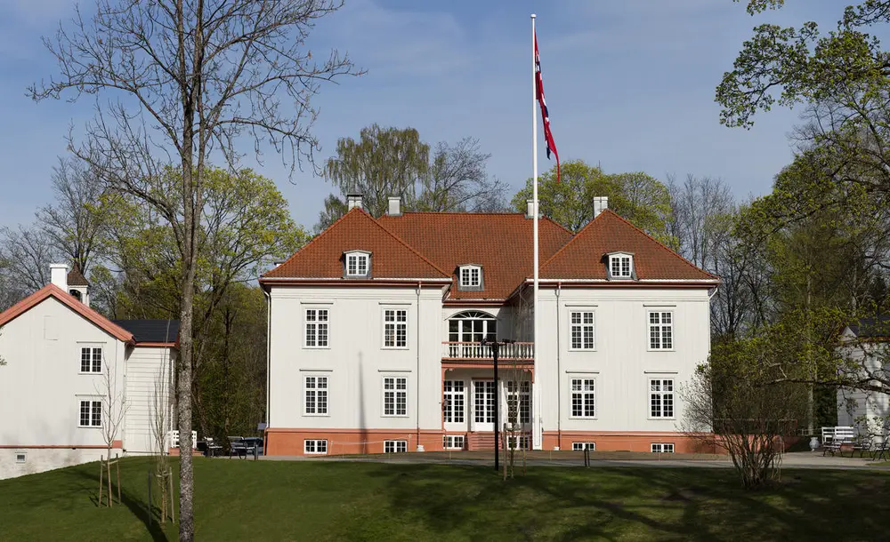 Eidsvollsbygningen, hovedfasade, flagg i flaggstanga og grønt i parken