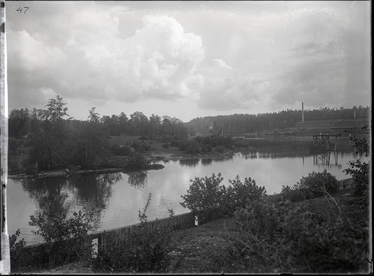 Fotografi taget i samband med byggandet av Södertälje kanalverk. I bakgrunden syns en industri samt en pråm och möjligen en flytande ångdriven grävskopa.
