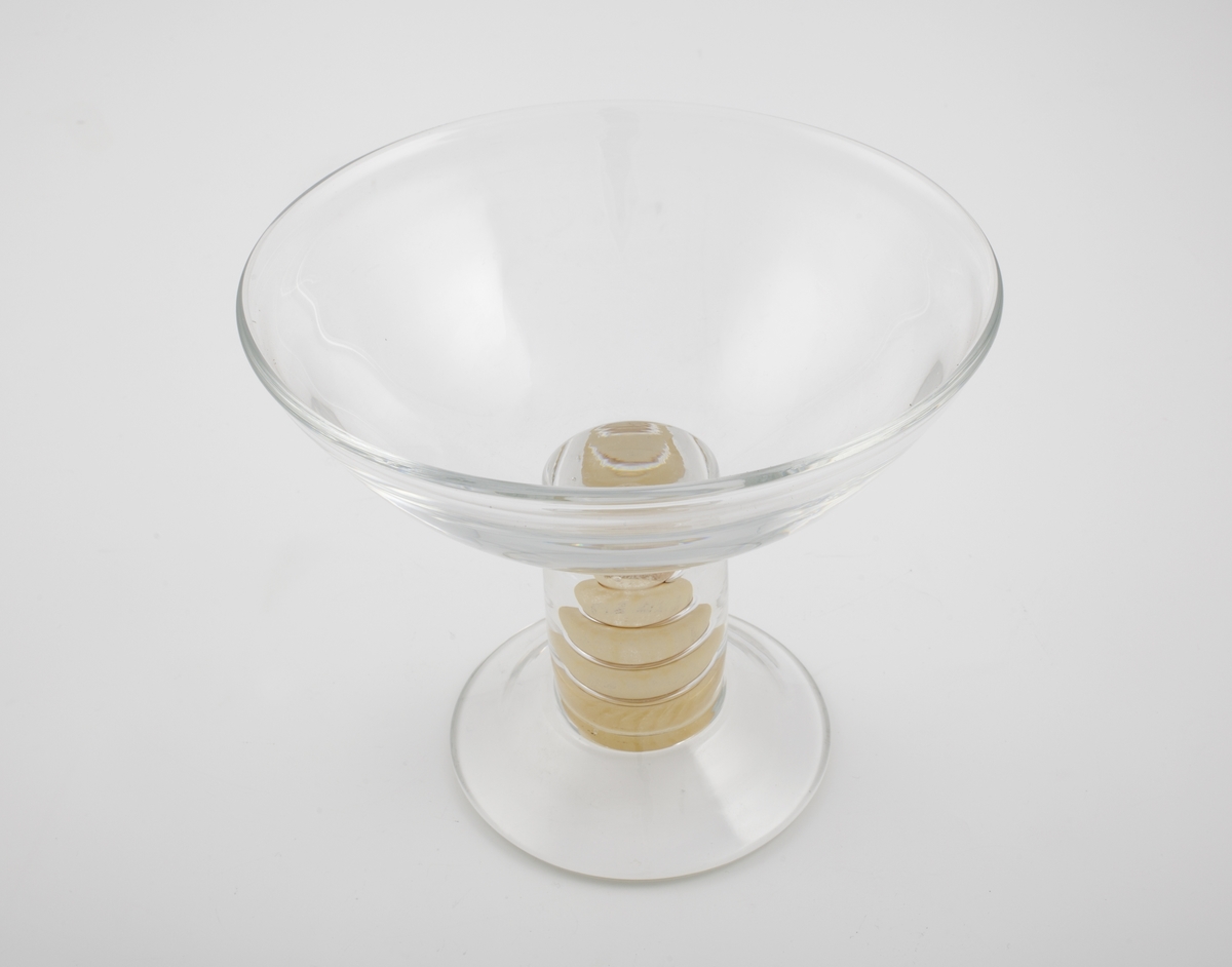 Vase i klart glass. Vid konisk kupa, som bæres av en massiv sirkulær stett. Stetten er dekorert med en spiral i halvgjennomskinnelig sandfarget glass, og hviler på en hevet fotplate.