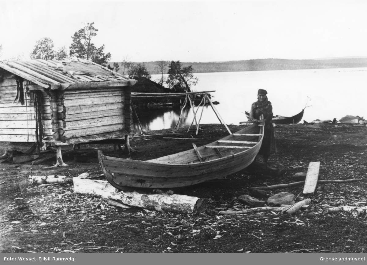 Kvinnelig båtbygger med sin nybygde skoltebask, østsiden av Borsejávri, Pasvik ca 1899. Et reinskinn ligger utspent på taket av koia.
