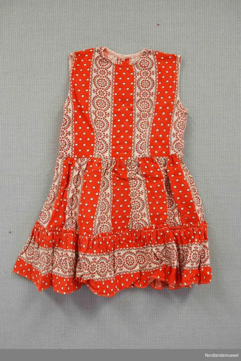 Mønstret kjole til barn. Oransje og hvitt mønster. Kappe nederst. Åpning bak med trykk-knapper.