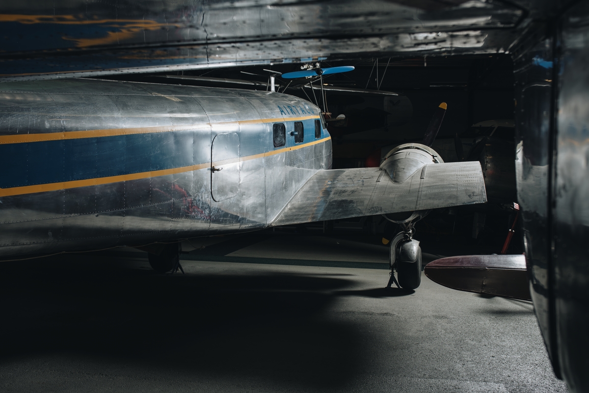 Flygplan av modellen Lockheed 12 Electra Junior. Propellerflygplan med metallren flygkropp och vingar, blå och gul dekor samt text: ”Airtaco AB”. Vänster vinge monterad, höger vinge ej monterad. Motorkåporna är till stor del ej original utan gjutna i plast. De passagerarstolar som är monterade är ej original, utan kommer från ett flygplan av typ DH 89 Dragon Rapide.