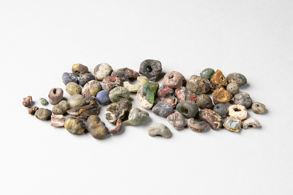 Pärlhalsband av glaspärlor samt 4 bronsspiralpärlor, vilka inte är fastsatta på halsbandet. Pärlorna är fasetterade, melon- och tunnformade och rikt ornerade i olika färger.