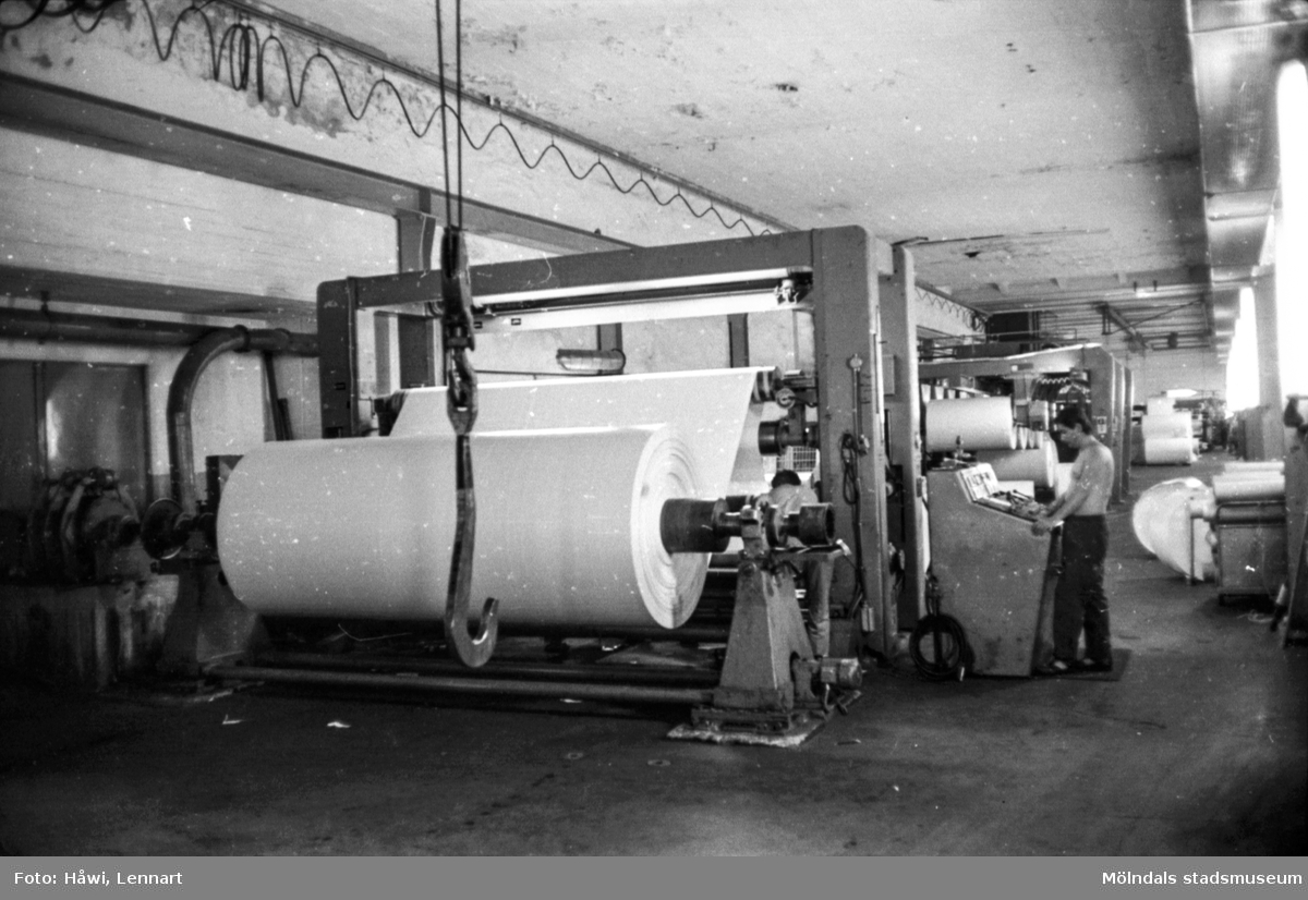 Man i arbete vid rullmaskin 5, byggnad 10 på pappersbruket Papyrus i Mölndal, hösten 1970. Mannen på bilden arbetar som rullare och sköter maskinen med hjälp av manöverbord.