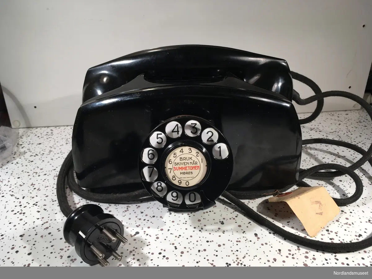 Telefonapparat med sveiv og nummerskive
Kombimodell, som kan benyttes i manuelt og automatisk telefonnett.
Bunnplate merket med AD 51775
Merkelapp på ledning merket med: "2. nov 1951" og "MEURICE BRUXELLES"
Produsent er noe usikker.