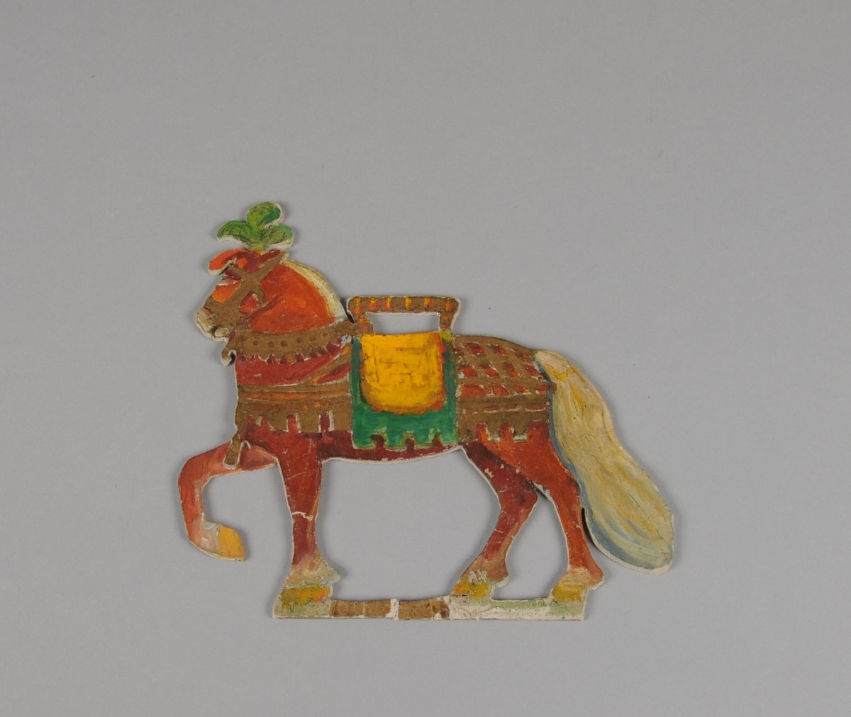 Figur av papp. Forestiller stående hest med fremre hov løftet. Hesten er farget rød.