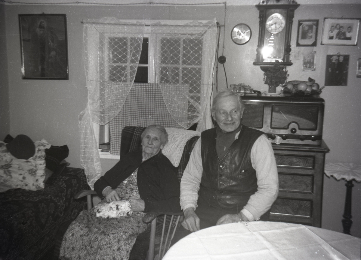 Portrettfotografi av ei eldre kvinne og mann i ei stue.
