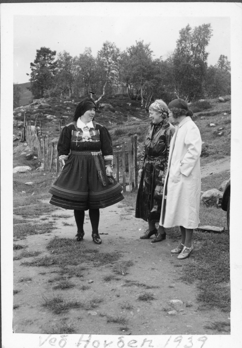 To kvinnelige turister snakker med kvinne i setesdalsbunad, 1939.