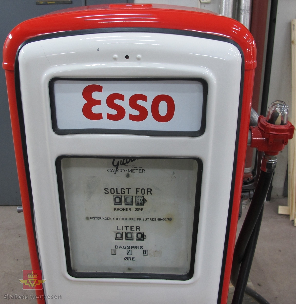 Rød og hvit drivstoffpumpe med Esso logo. Elektrisk drevet, med telleverk og gummislange med pumpepistol. Pumpen har flere merkinger og innskrifter: GILBARCO MADE IN ENGLAND MANUFACTURED BY VICKERS ARMSTRONG LTD GRAYFORD KENT UNDER LISENCE OF GILBERT & BARKER MANF. CO TRADEMARK DISTRIBUTED BY STEMCO LTD CAMDEN TOWN N. W. I.  Gilbarco REGISTRERT VAREMERKE CALCO-METER  MINSTE TILLATTEMÅLEKVANTUM.5L  3 2 ÅRLIG REVISJONSPLIKT 59 63 66 68 71 73 E86 JK.1 NR. TOTALTELLEVERKET IKKE JUSTERT.