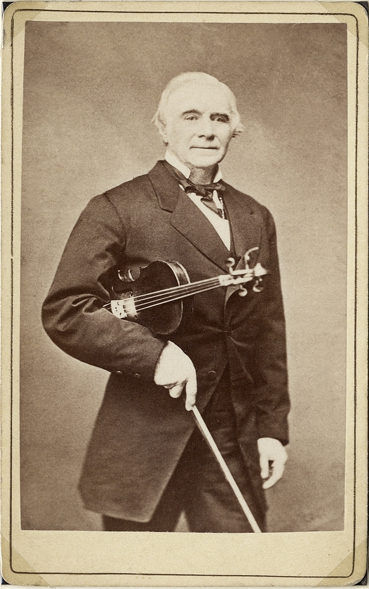 Porträttfoto av en man i bonjour med stärkkrage och fluga, Han håller en fiol under armen. 
På baksidan text: "Ch. Bull" (?). 
Bröstbild, halvprofil. Ateljéfoto.