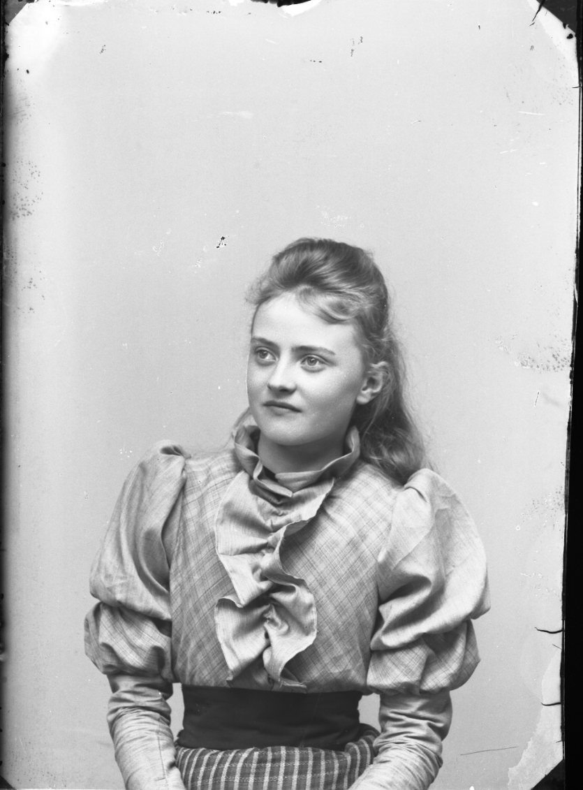 Porträtt av Ester Grönberg. Hon bär en svagt mönstrad blus med krås på bröstet och rutig klänning.