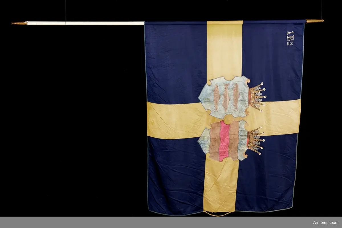 Duk av blått och gult siden med Västernorrlands heraldiska vapen bestående av Ångermanlands och Medelpads vapen i varsin sköld krönta med hertigkronor. I övre stångsidan broderat 1 Bn (första bataljonen).