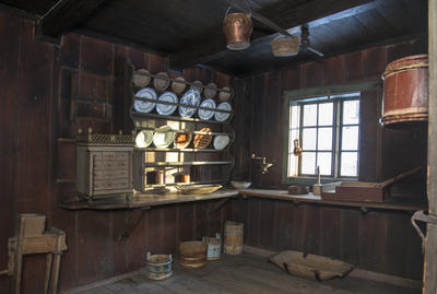 Interiør fra kjøkkenet i Skøienbygningen som viser en fullsatt tallerkenhylle i fire høyder og lyset som faller inn på porselenet gjennom et smårutete vindu.