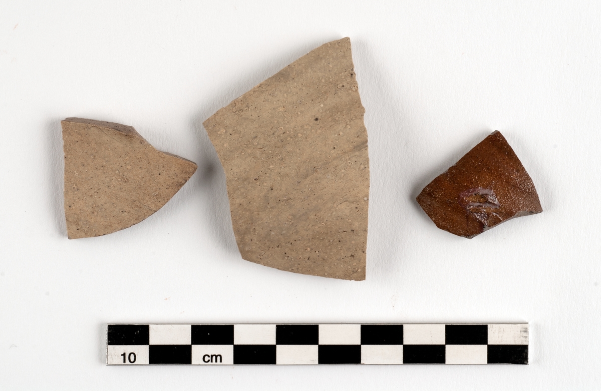 Del av kärl. Bukfragment av kärl i stengods. Langerwehe. Nästan genomsintrat. Datering troligen 1400-1500-tal. (Fragmentet längst till höger på bilden.)