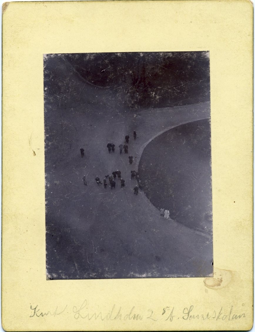 Foto från ballongen Sveas gondol (förankrad) ned mot marken där en grupp människor står samlade.