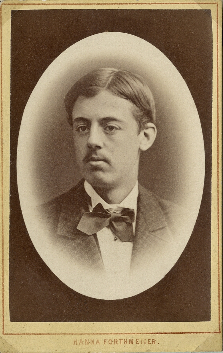 Porträttfoto av en ung man i kavajkostym med stärkkrage m.m.
Bröstbild, halvprofil. Ateljéfoto.