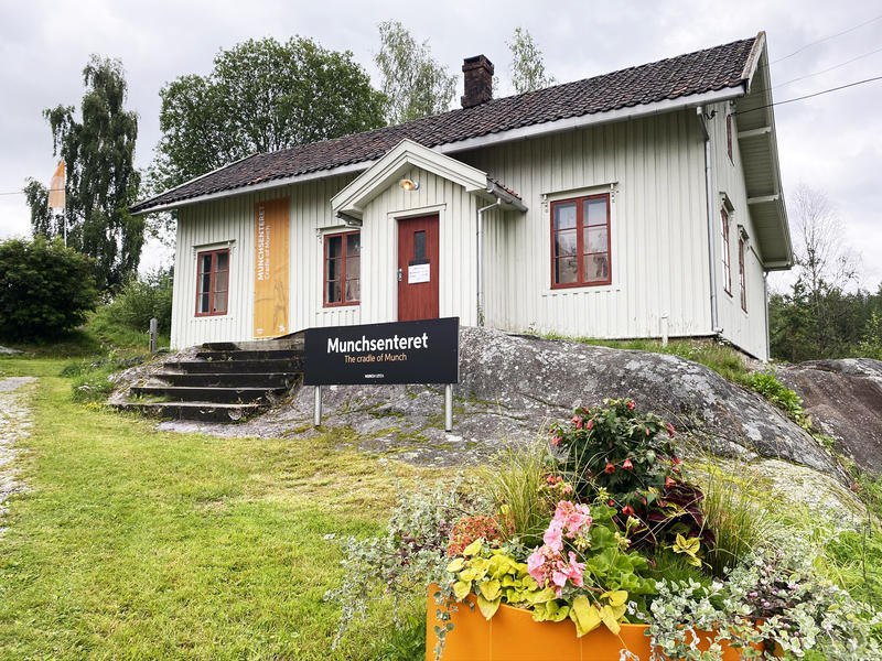 Munchsenteret i Løten, hvit trebygning med grønn plen og blomster i forgrunnen