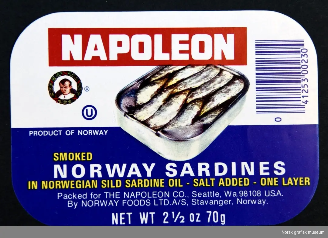 Etikett med hvit og mørkeblå bakgrunn. Midt på er en fremstilling av en åpnet hermetikkboks. 

"Smoked Norway sardines in Norwegian sild sardine oil"