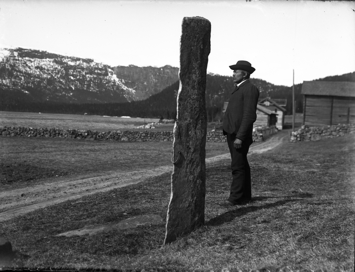 Fotosamling etter Bendik Ketilson Taraldlien (1863-1951) Fyresdal. Gårdbruker, fotograf og skogbruksmann. Fotosamlingen etter fotograf Taraldlien dokumenterer områdene Fyresdal og omegn. 
Portrett av Jørund Bondal som står ved den høye steinen.