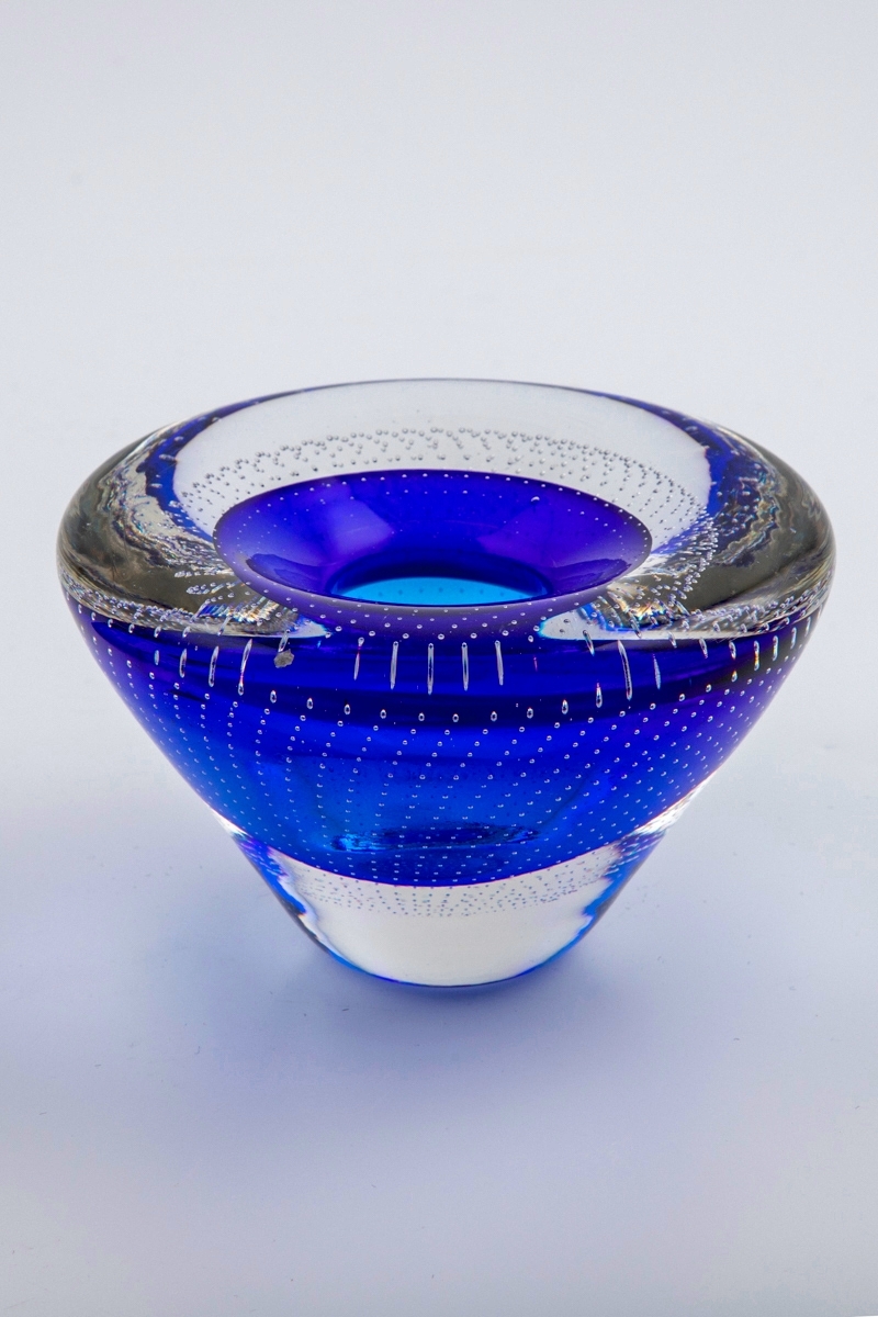 Vase i underfangsglass. Konisk form med et blått sjikt rundt munningen, omgitt av en klar glassmasse. Konkavt toppstykke med liten sirkulær åpning. Korpus er dekorert med små radiale luftbobler som er innlagt i glassmassen.