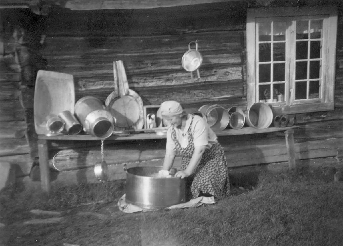 Margit Illevold var i mange år budeie på Illvålsetra i Jota, oppi Nordstu'n som het i setergrenda. Her rører hun i mussmørkjelen. Skinnende rene mjølkespann og utstyr ellers til tørk i solveggen. 
