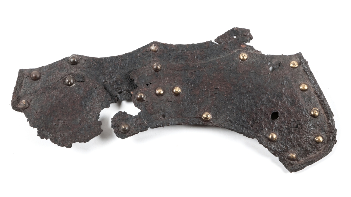 Harnesk, fragment. Delarnas sammanlagda bredd 34 cm. Av järn med mässingsnitar. Troligen delar som suttit upptill på bröstet. jordfynd.