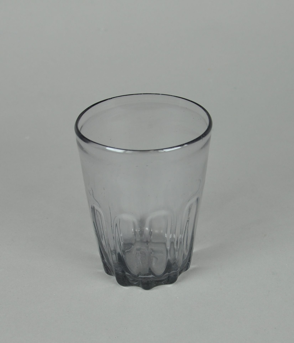 Blåst ølglass. Sylindrisk glass, med dekorative innsnevringer ved bunn. Innsnevringene er rektangulære, med avrundet topp.