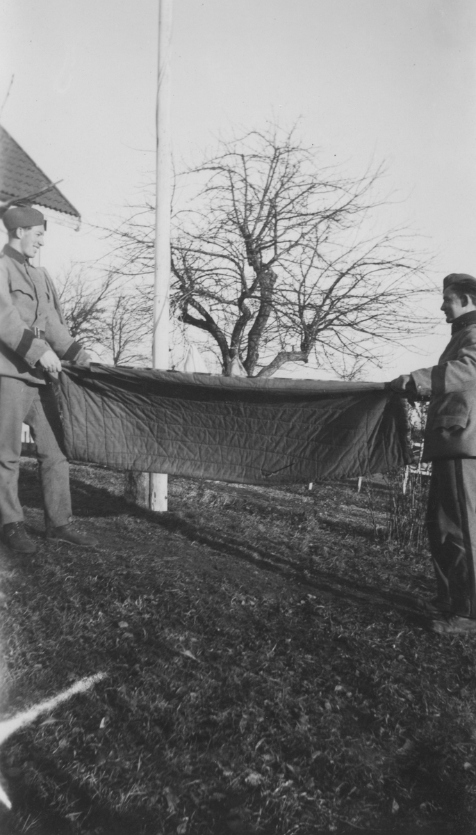 Vädring av täcke, utomhus. Två frivilliga luftbevakare från landstormsregemente L 2 i Dalsland under beredskapstiden skakar ett täcke.